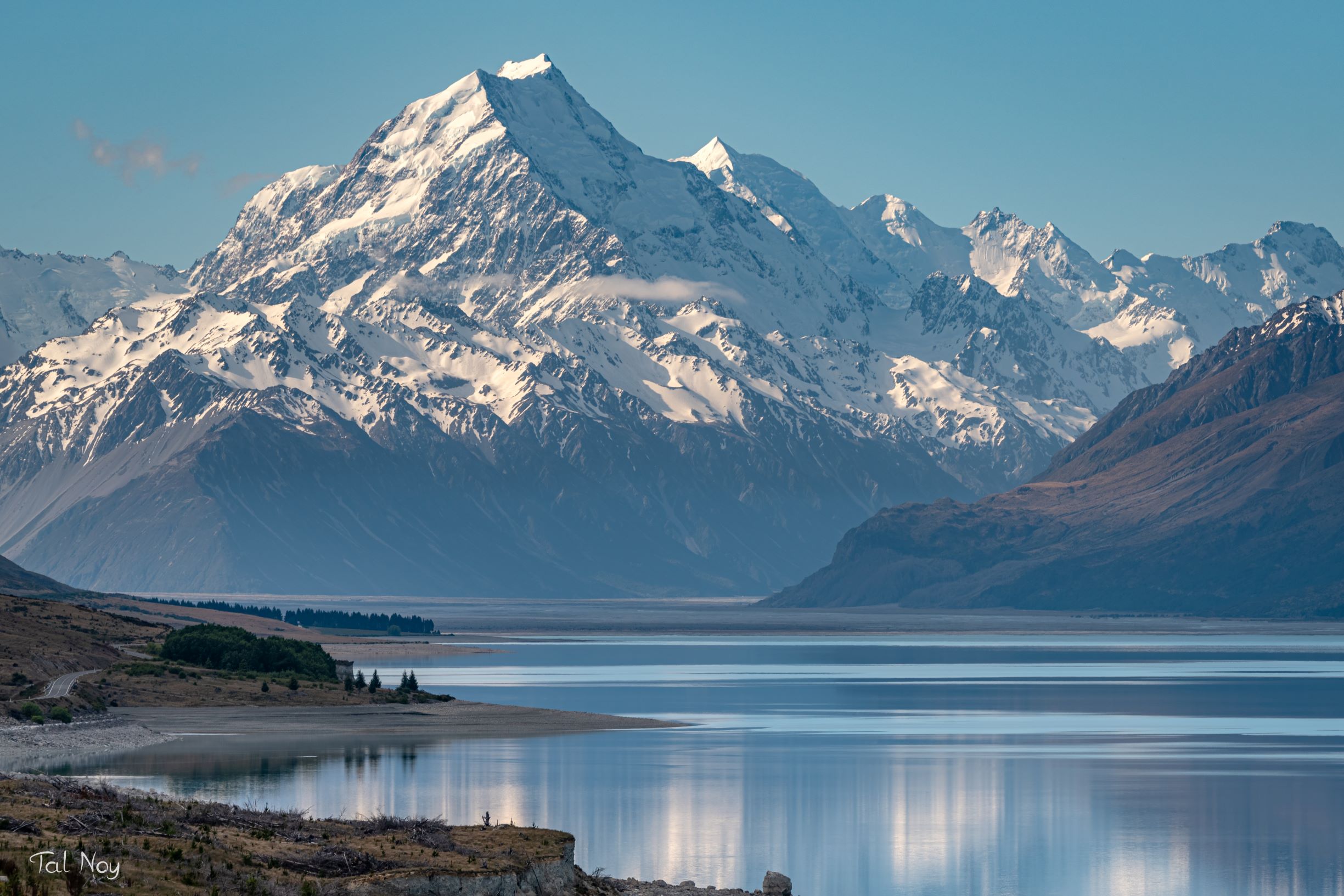 Mount Cook reflected in a calm lake, captured with a telephoto lens to emphasize the mountain's immense scale