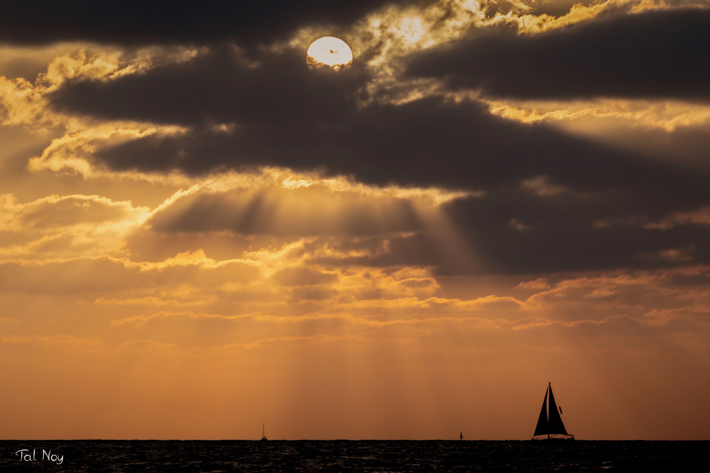 Silhouette of a sailboat beneath sun rays breaking through clouds before sunset, Israel
